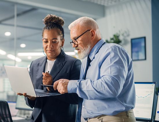 A woman holding a laptop whilst a man looks at what is on the laptop's screen