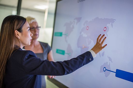 Two people looking at a screen with a map of the world on it, one of them is explaining what the map demonstrates.